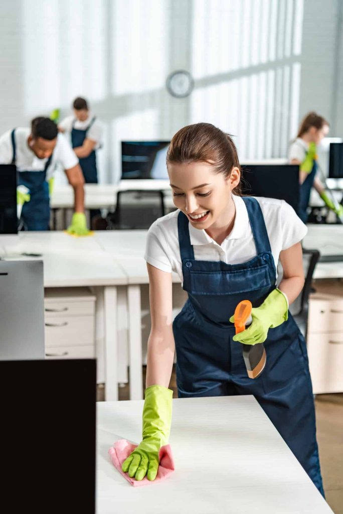 Cheerful cleaner wiping an office desk with care